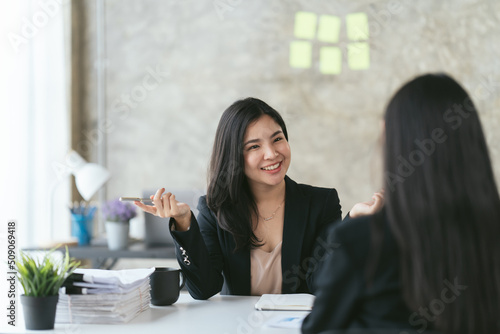 Group of young asian business people discussing something and smiling while sitting at the office table, two business people in the office working together. photo