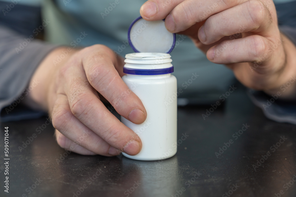 An adult man holds a white vial in his hands. An adult man holds a white vial in his hands.