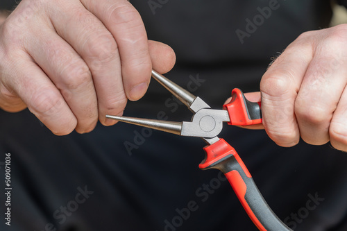 The hand of a mature man holding round pliers. Hand-held locksmith tool with smooth surface finish and diameter tapering toward the tips.