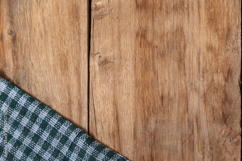 A green checkered cloth lies against a wooden background. A towel or kitchen napkin on the rough boards or kitchen table.