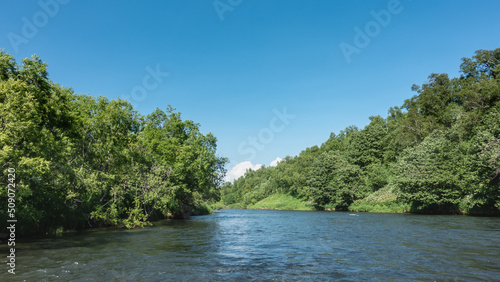 The bed of the calm river bends. The banks overgrown with lush green vegetation. Clear blue sky. Copy space. Kamchatka.