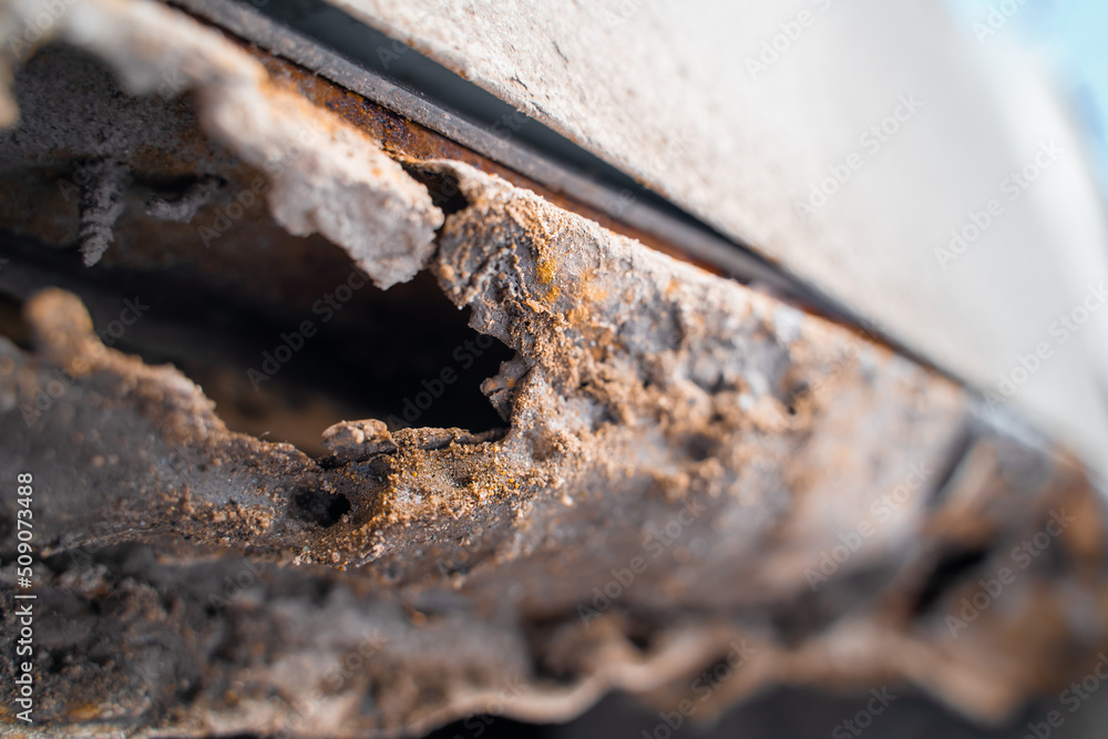 Fototapeta premium Rusted through the bottom of the door of a white car close-up