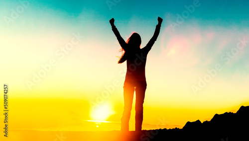 Happy woman sihouette with arms up for life success celebrating financial freedom early retirement on sunset glow sun at mountain summit. Wellness, healthy concept background. Goal achievement