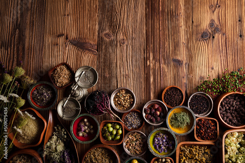  Natural medicine background. Assorted dry herbs in bowls and brass mortar on rustic wooden table.