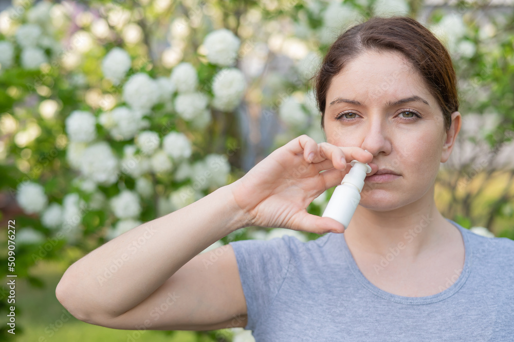 Caucasian woman uses a nasal spray while walking in the park. Caucasian woman uses a nasal spray while walking in the park.