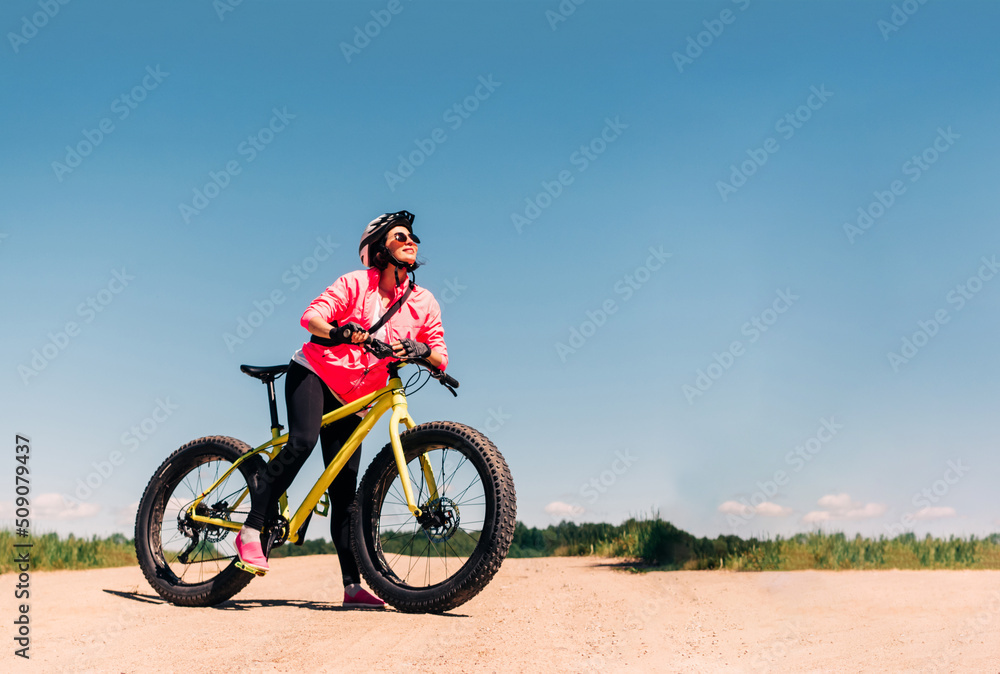 Fat-tire bike in summer driving through the hills. Woman is posing with a fat bike in the forest. She performs some tricks and runs dangerously. Bicycle with thick wheels in nature.