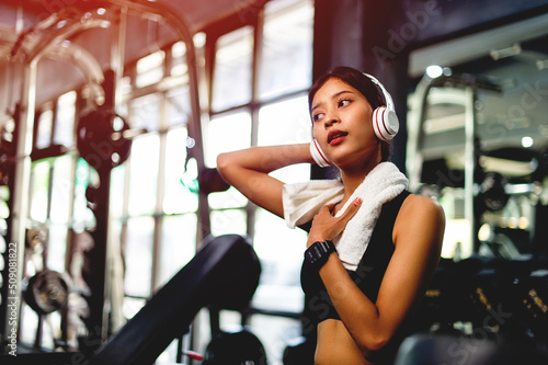 girl in the gym exercising Using a mobile phone, listening to music with white over-ear headphones and using a digital heartbeat timer. systematic exercise her vacation relaxation
