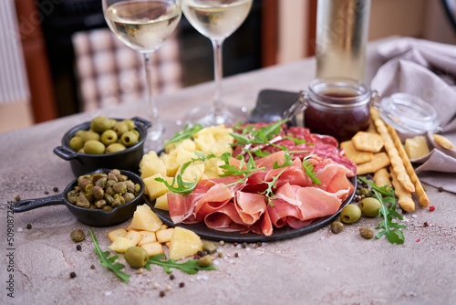 Two glasses of white wine and Italian antipasto meat platter on domestic kitchen