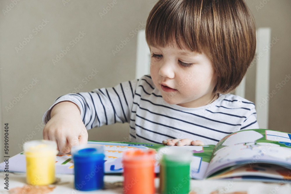 Finger painting. Portrait of cute little boy painting with fingers at home. Close-up of child's hand in colorful paints. Early education concept. Sensory play. Development of fine motor skills. Finger painting. Portrait of cute little boy painting with fingers at home. Close-up of child's hand in colorful paints. Early education concept. Sensory play. Development of fine motor skills.