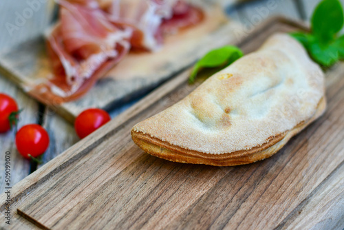 Home made italian calzone pizza with tomatoes, prosciutto mozzarella and parmesan cheese and fresh basil 