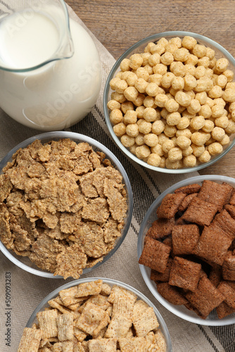 Different breakfast cereals and milk on wooden table, flat lay