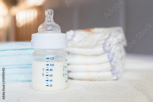 Baby bottle with milk and diapers on a white fabric background. Baby care. First days of life. Feeding and motherhood