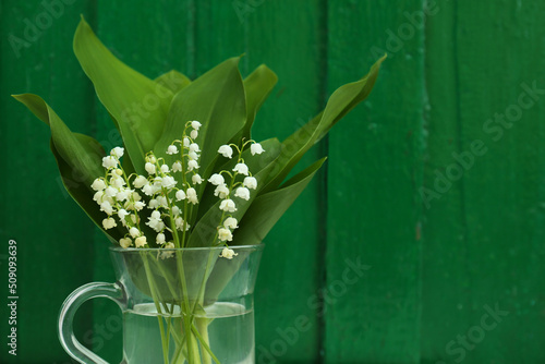 Beautiful lily of the valley flowers on green wooden background. Space for text