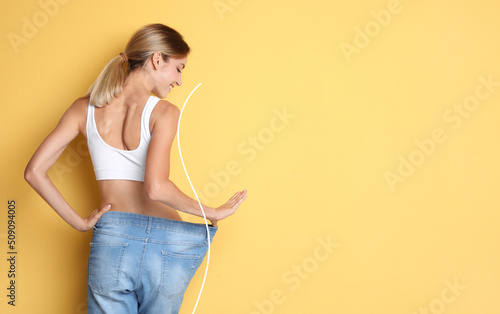 Happy young woman with slim body in oversized jeans on yellow background, space for text. Weight loss