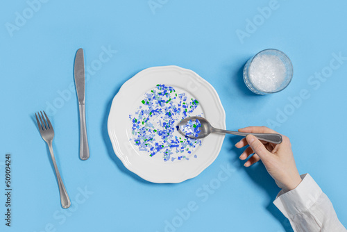 Plate with plastic pieces instead of food and glass of microplastics instead of water. Microplastic problem concept, ocean pollution ecology problem, environmental impact on nature, top view photo