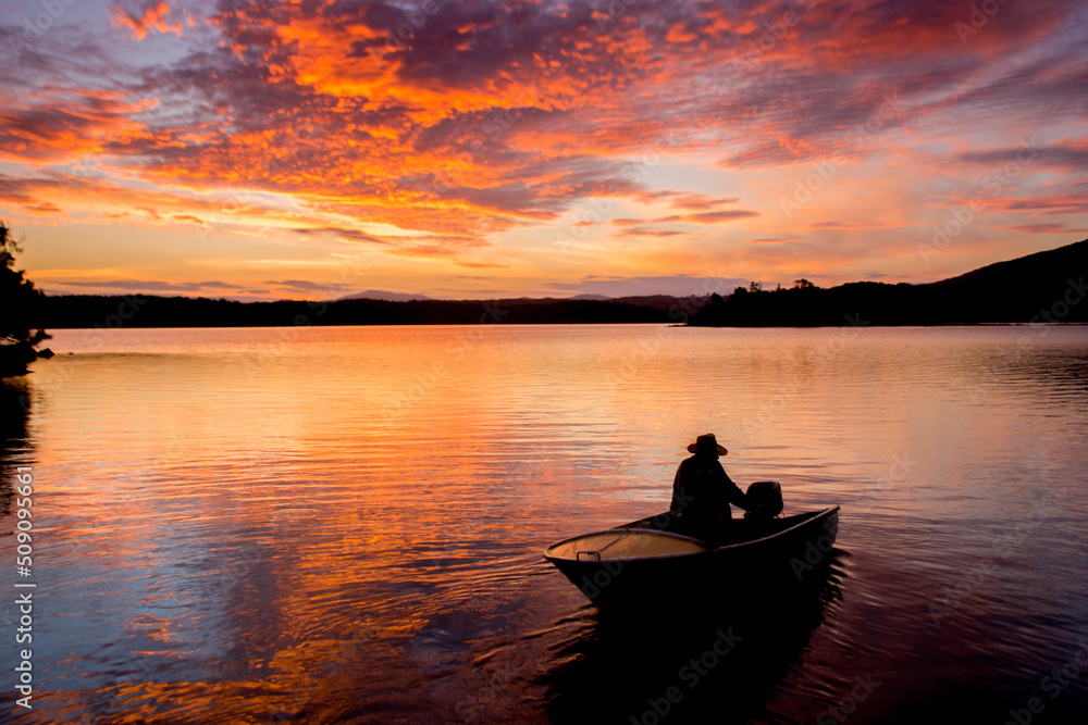 Beautiful sunset on tranquility lake with fishing boat silhouette. Water reflections nature background