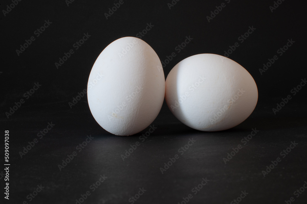 Two eggs, profile view of white raw chicken eggs isolated on dark background, selective focus. Two eggs, profile view of white raw chicken eggs isolated on dark background, selective focus.