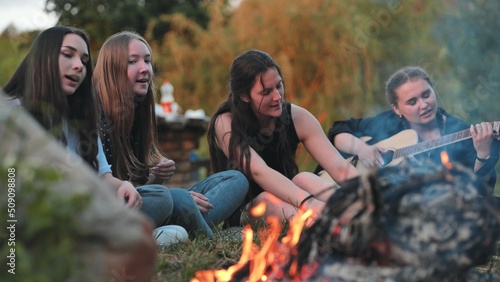 A group of friends with a guitar are sitting around the fire in the evening.