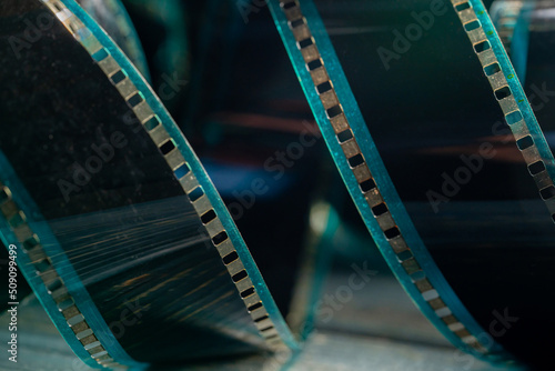 Spiral retro film strip on wooden surface in soft green light. Twisted analog old strips of film for photo or video camera close up. The concept of cinematography, photography, photographic memories.