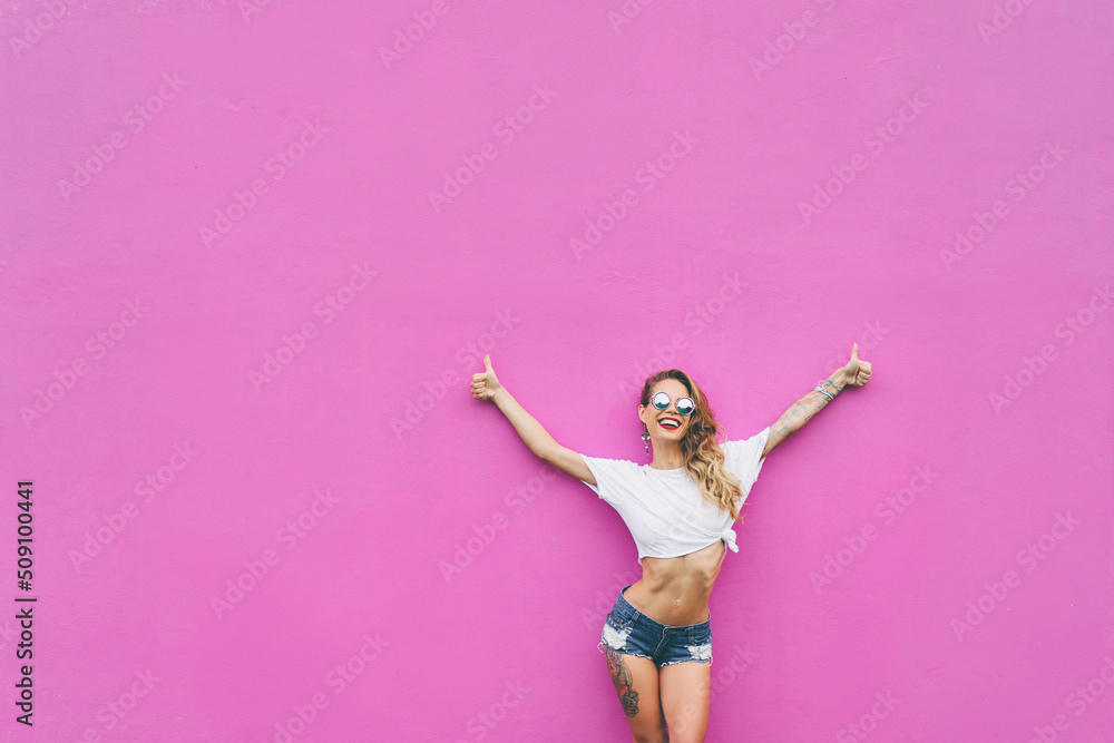 The best! Young pretty smiling woman rising hands with thumbs up against pink wall. The best! Young pretty smiling woman rising hands with thumbs up against pink wall.