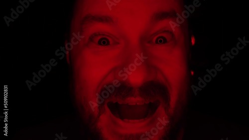 The evil laugh of an unshaven man illuminated by red light.