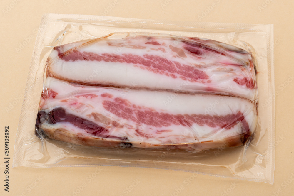 Italian Guanciale, slices dry cured pork cheek in in vacuum packed sealed for sous vide cooking isolated on light brown background Italian Guanciale, slices dry cured pork cheek in in vacuum packed sealed for sous vide cooking isolated on light brown background