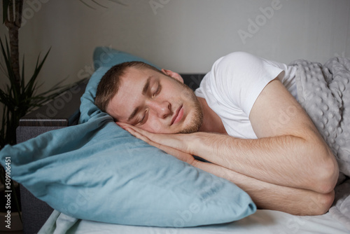 Man sleeps in bed with his hands under his head