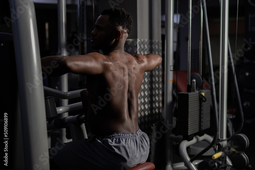 Shirtless african american man doing back exercises on a machine in the gym.