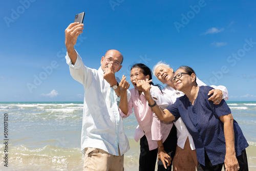portrait senior man and women taking selfie and mini heart pose from smartphone on the beach