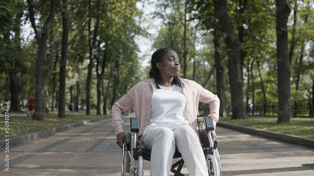 Unhappy African woman with disability sitting in wheelchair, alone in park Unhappy African woman with disability sitting in wheelchair, alone in park