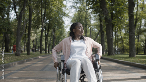 Unhappy African woman with disability sitting in wheelchair, alone in park