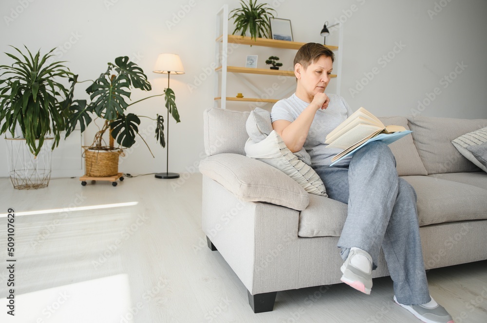 Middle-aged housewife sitting on sofa with book, free time retirement, hobby. Middle-aged housewife sitting on sofa with book, free time retirement, hobby.