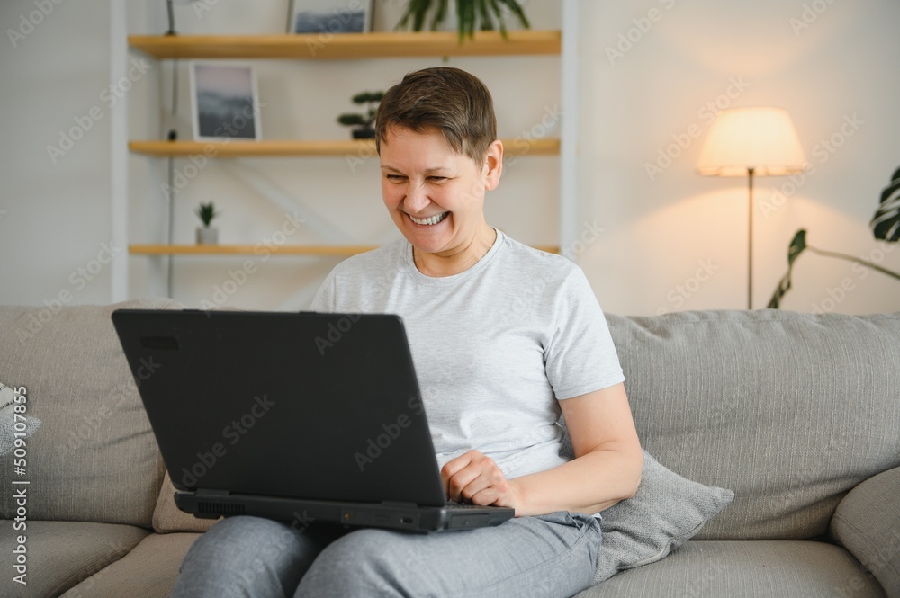Elderly female sit on couch holding on lap laptop search information, check or typing e-mail, spend time on-line, modern tech, easy interesting pastimes services for retired older generation concept.