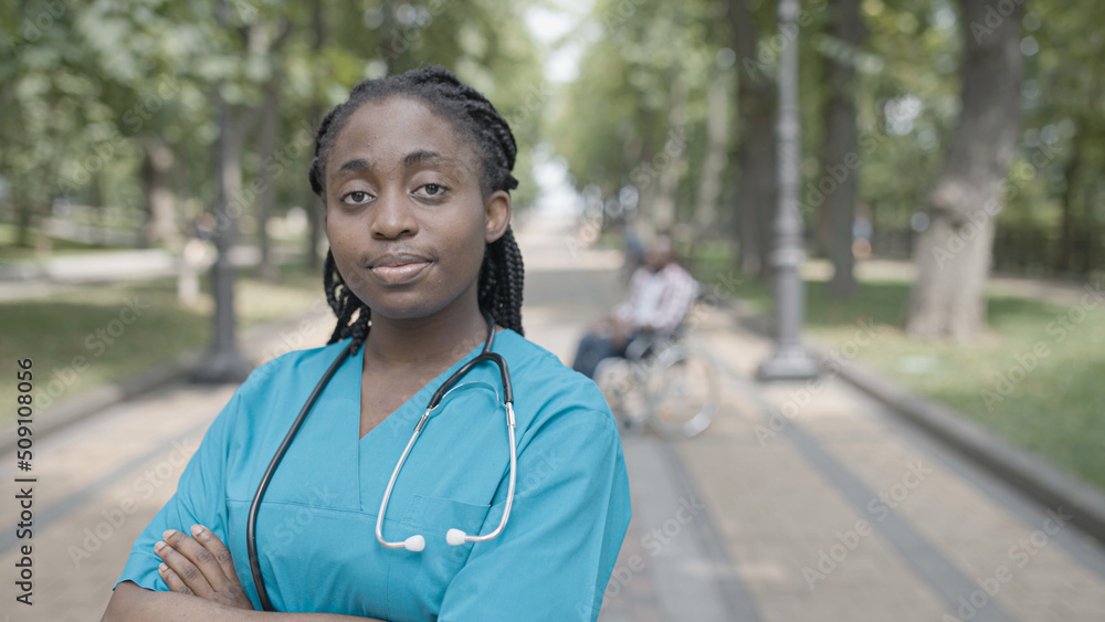 Confident female doctor crossing arms on chest and smiling on camera in park Confident female doctor crossing arms on chest and smiling on camera in park