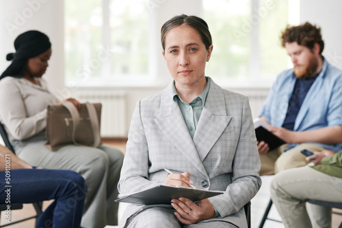 Wallpaper Mural Young confident female counselor in elegant grey suit holding document while sitting in front of her patients and looking at camera Torontodigital.ca