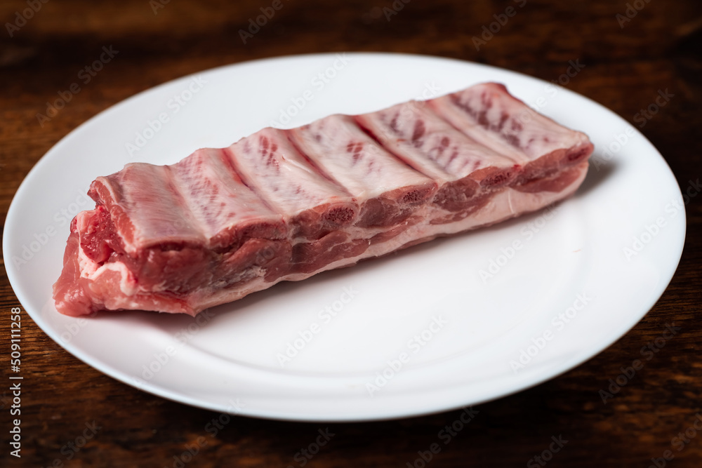 Fresh raw meat and pork ribs on a white plate on a wooden background.
