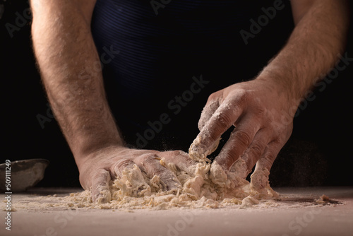 Cooking, kneading dough. Male hands mix the ingredients for the dough on the table against a dark background.