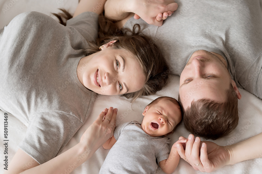 Newborn baby in mother's and father's arms on bed. Postcard Mother's and father's day. Children Protection Day. World Happiness Day. Smiling child. Happy parenthood