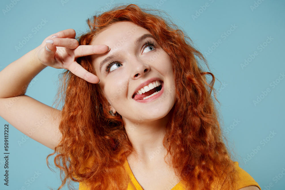 Close up young redhead woman 20s wearing yellow t-shirt doing selfie shot pov on mobile cell phone show v-sign isolated on plain light pastel blue background studio portrait. People lifestyle concept. Close up young redhead woman 20s wearing yellow t-shirt doing selfie shot pov on mobile cell phone show v-sign isolated on plain light pastel blue background studio portrait. People lifestyle concept.