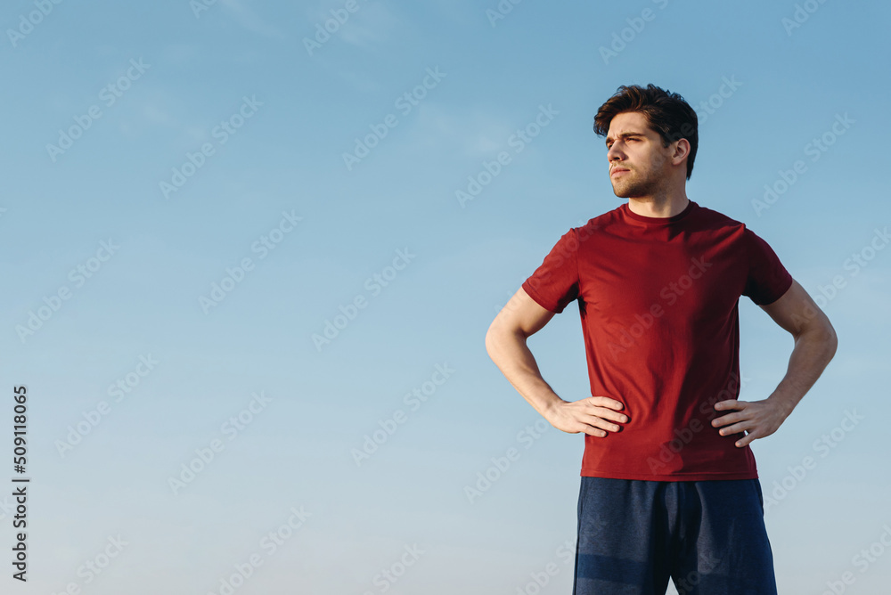 Bottom view young strong sporty athletic toned fit sportsman man 20s wear sports clothes stand akimbo look aside warm up training at sunrise sun dawn over sea beach outdoor on pier seaside in morning. Bottom view young strong sporty athletic toned fit sportsman man 20s wear sports clothes stand akimbo look aside warm up training at sunrise sun dawn over sea beach outdoor on pier seaside in morning.