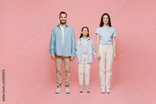 Full body young happy cool caucasian smiling fun cool parents mom dad with child kid daughter teen girl in blue clothes hold hands isolated on plain pastel light pink background. Family day concept.