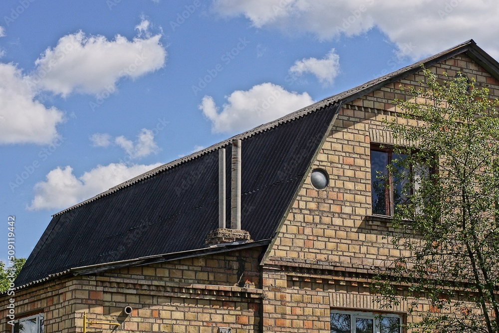 two gray chimneys on the slate roof of a brown brick private house with windows against a blue sky two gray chimneys on the slate roof of a brown brick private house with windows against a blue sky
