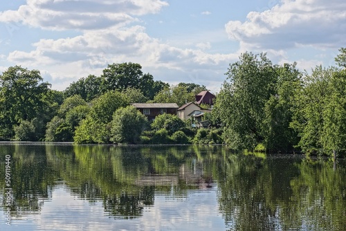  landscape from the water of the lake against the background of green trees of private houses and a blue sky