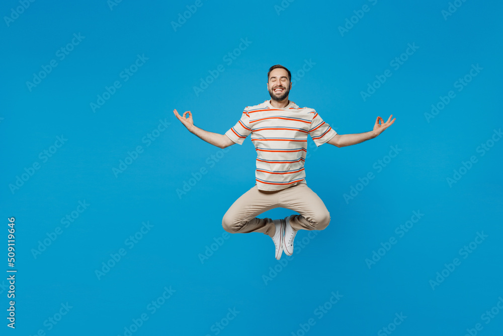 Obraz premium Full body young smiling man 20s wear orange striped t-shirt hold spreading hands in yoga om aum gesture relax meditate try to calm down levitating isolated on plain blue background studio portrait
