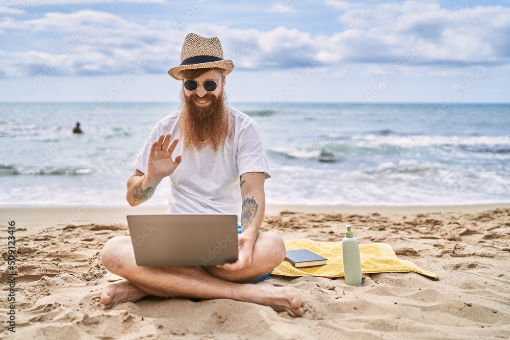 Young redhead man having video call using laptop at the beach.