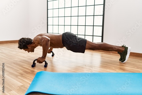 Slika na platnu Young african american man training push-ups at gym