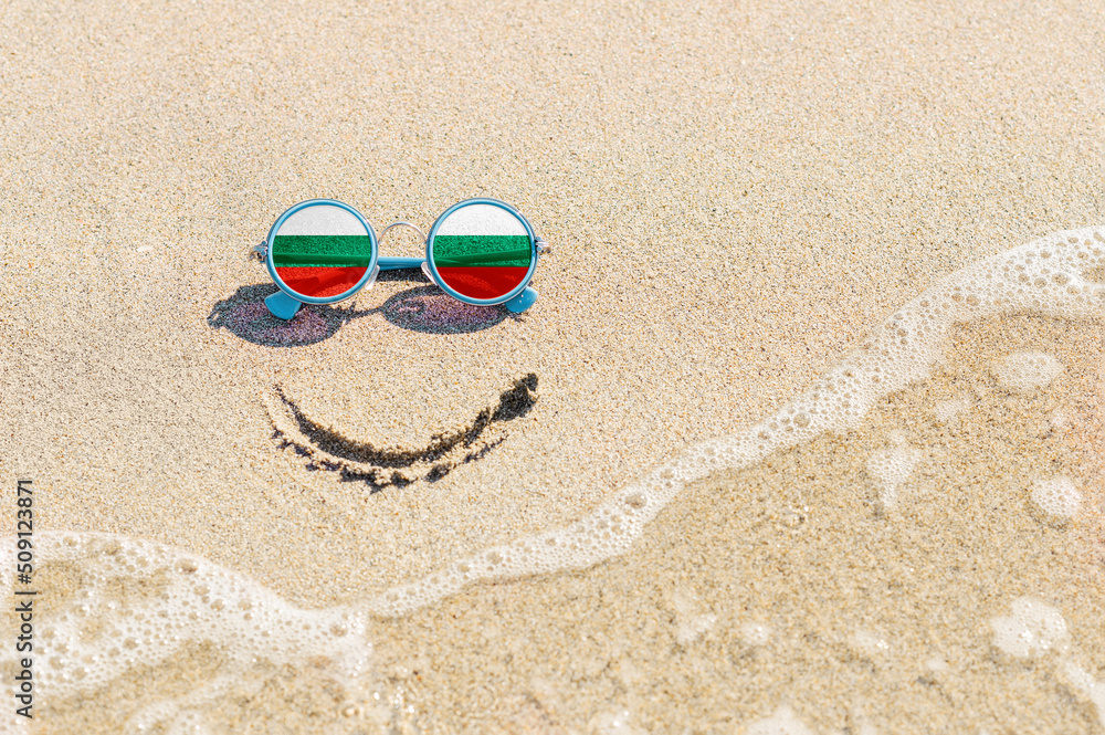 Obraz premium A painted smile on the beach and sunglasses with the flag of the Bulgaria. The concept of a positive holiday in the resort of the Bulgaria.