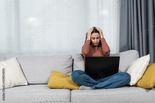 Young student or business woman sitting at home covering her ears with hands because she cant study or work on her laptop computer from loud noise coming from apartment above.