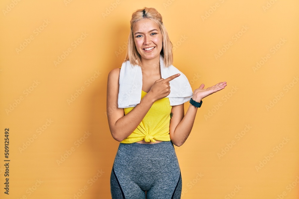 Beautiful blonde sports woman wearing workout outfit amazed and smiling to the camera while presenting with hand and pointing with finger. Beautiful blonde sports woman wearing workout outfit amazed and smiling to the camera while presenting with hand and pointing with finger.