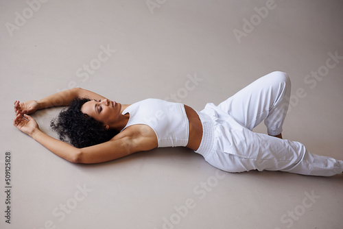 Sexy curly woman doing stretching on white background. Young girl in white clothes isolated